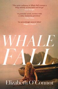 Book cover, Whale Fall by Elizabeth O'Connor. A woman sitting on the shore by a boat with mountains in the background.